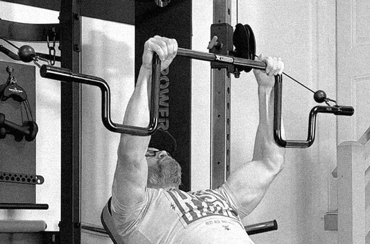 HGHR doing a pullover lat exercise on a functional trainer with the Andreoni bar attachment in black and white photo